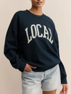 Person wearing a navy sweatshirt with 'LOCAL' printed on it against a beige background