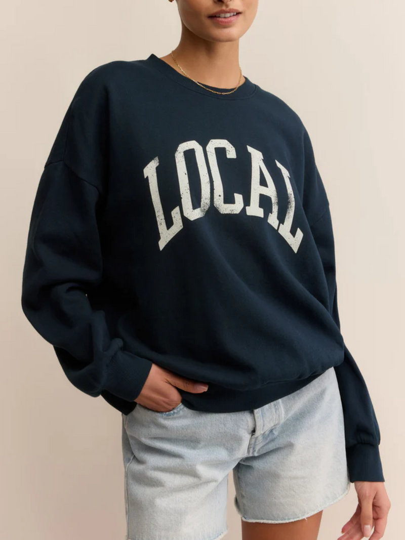 Person wearing a navy sweatshirt with 'LOCAL' printed on it against a beige background
