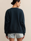 Person wearing a dark blue sweatshirt and light denim shorts on a beige background
