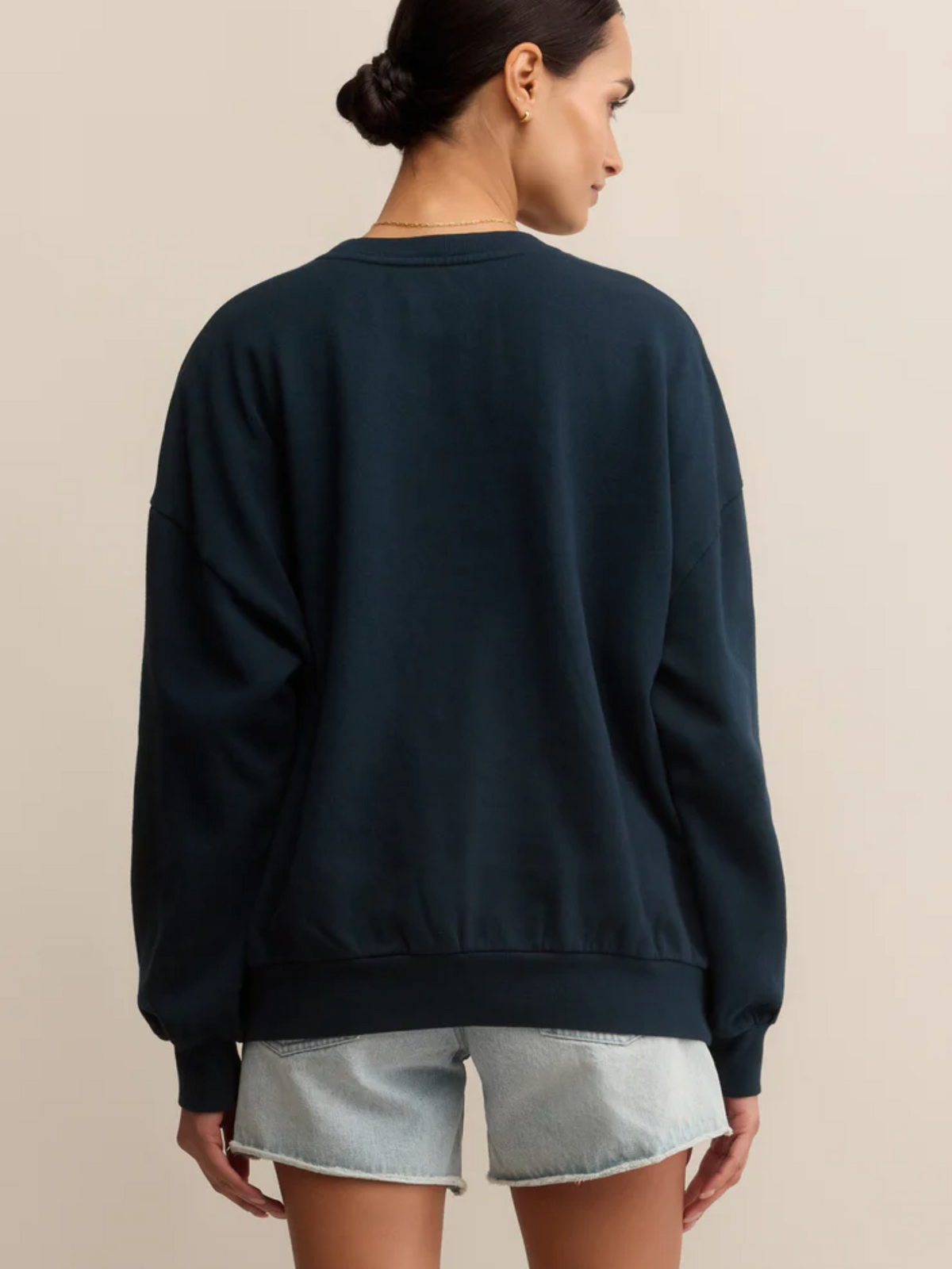 Person wearing a dark blue sweatshirt and light denim shorts on a beige background