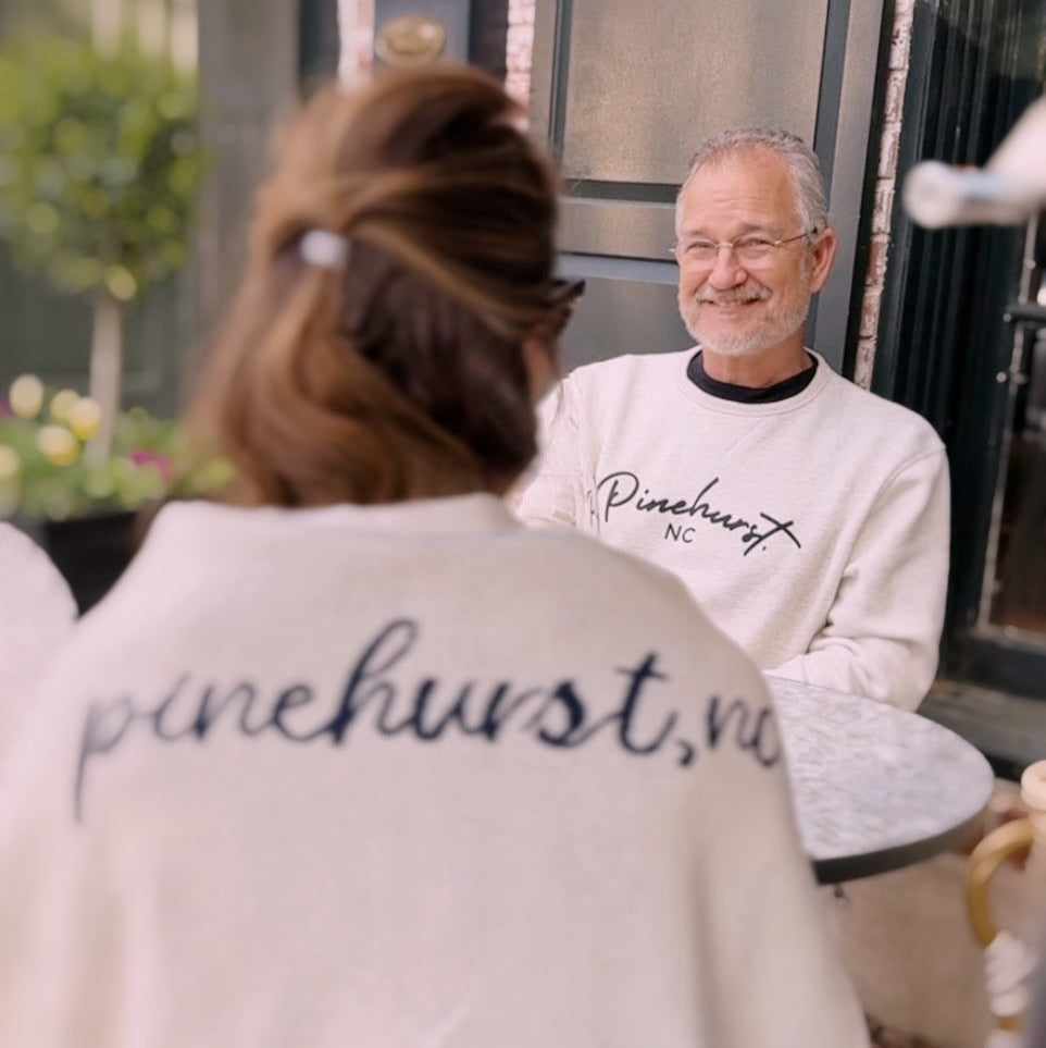 Two people sitting outdoors, both wearing 'Pinehurst' clothing.